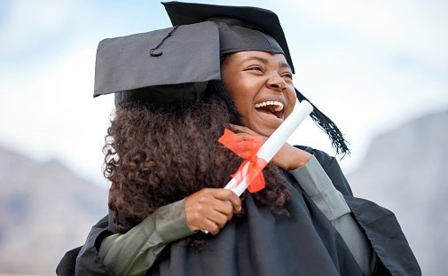 A graduate in cap and gown celebrating with a diploma