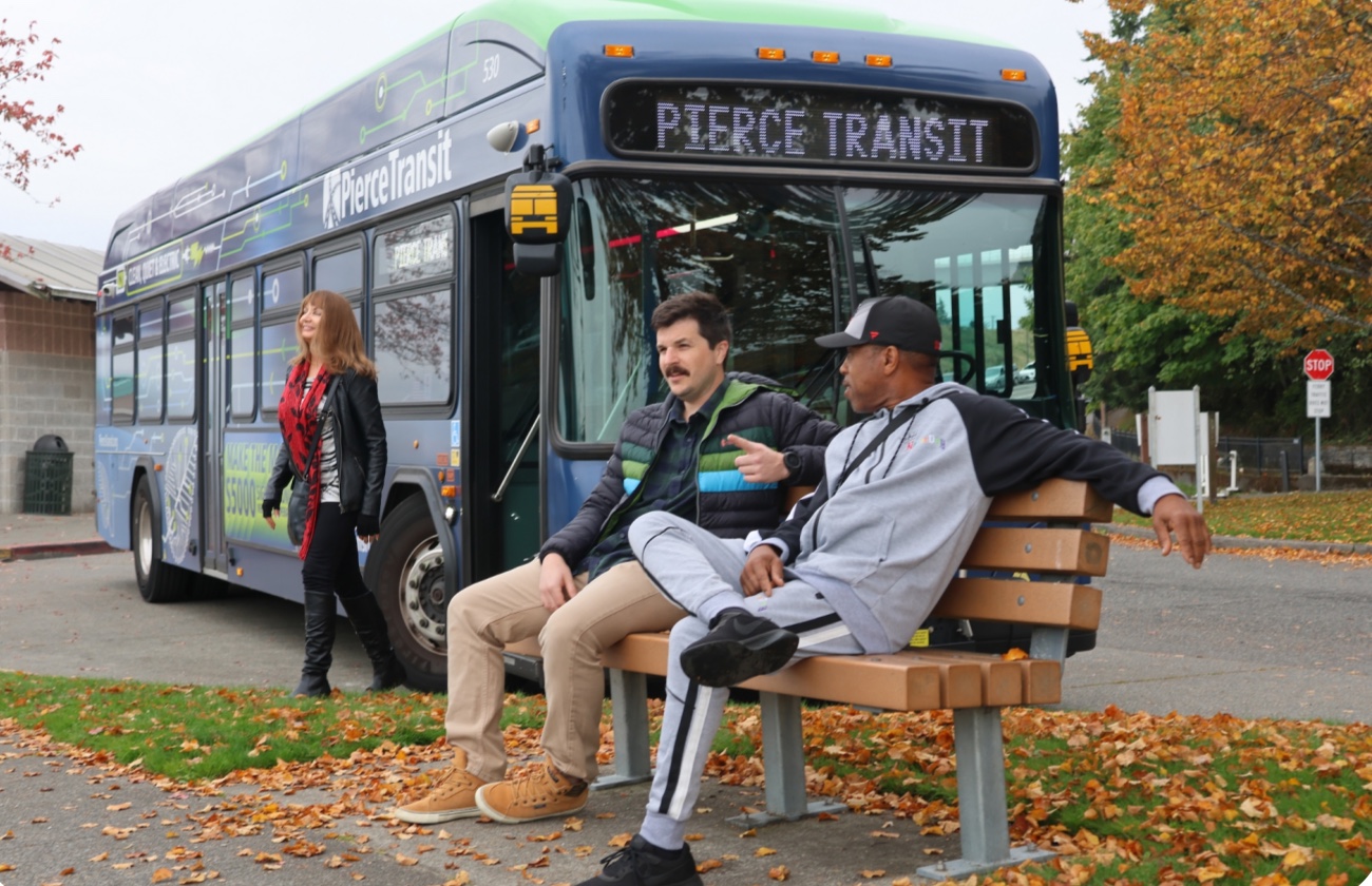 Riders waiting on a bench beside a Pierce Transit bus